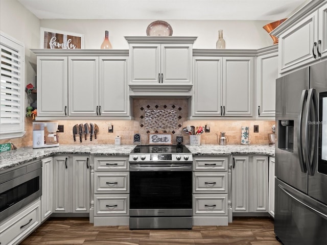 kitchen featuring stainless steel appliances, dark hardwood / wood-style floors, light stone countertops, and backsplash