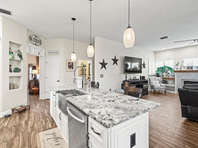 kitchen with pendant lighting, dishwasher, an island with sink, sink, and white cabinets