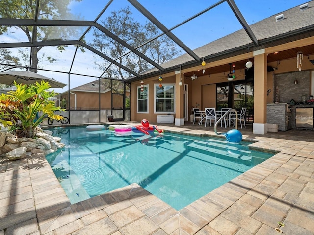 view of pool with area for grilling, a patio, glass enclosure, and ceiling fan