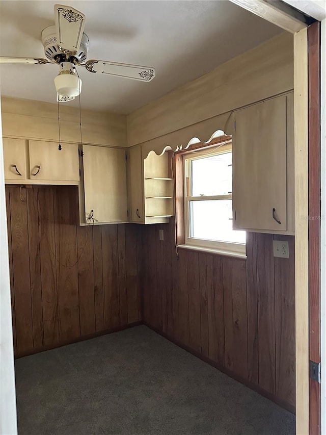 empty room featuring ceiling fan, wooden walls, and dark carpet