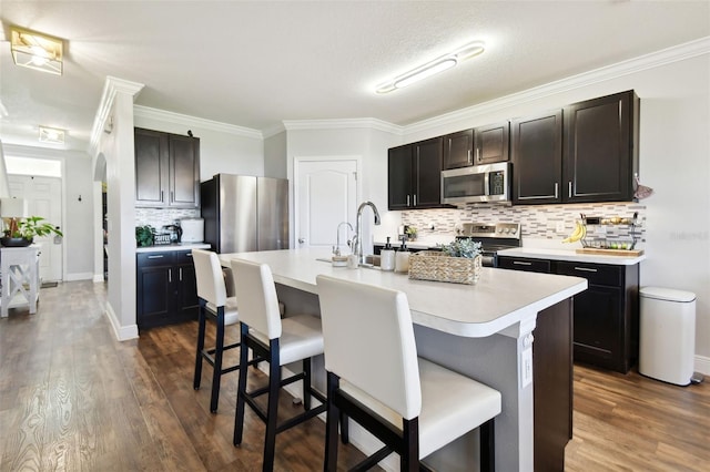 kitchen with decorative backsplash, appliances with stainless steel finishes, a kitchen breakfast bar, and a center island with sink