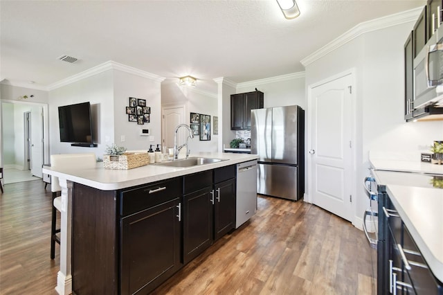 kitchen featuring appliances with stainless steel finishes, an island with sink, sink, a kitchen bar, and ornamental molding