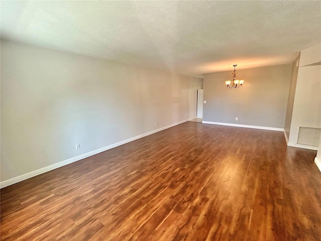 spare room with a notable chandelier, a textured ceiling, and dark hardwood / wood-style floors