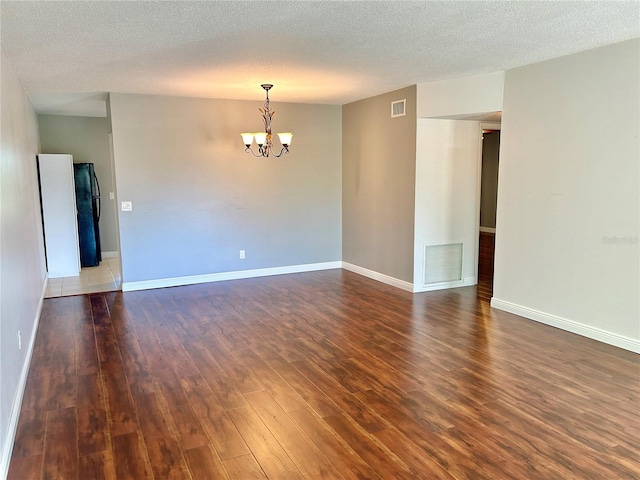 unfurnished room featuring dark wood-type flooring, a textured ceiling, and a chandelier