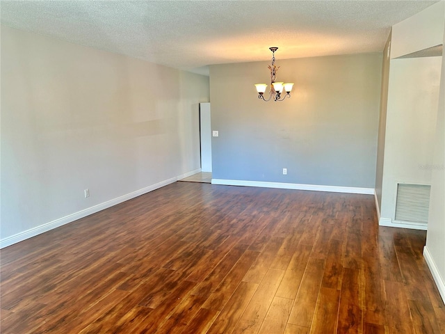 empty room featuring an inviting chandelier, a textured ceiling, and dark hardwood / wood-style floors