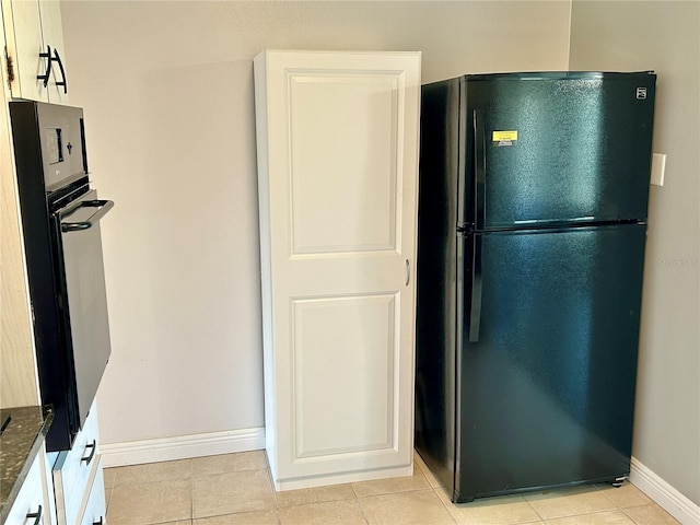 kitchen featuring oven, light tile patterned floors, white cabinetry, dark stone counters, and black refrigerator