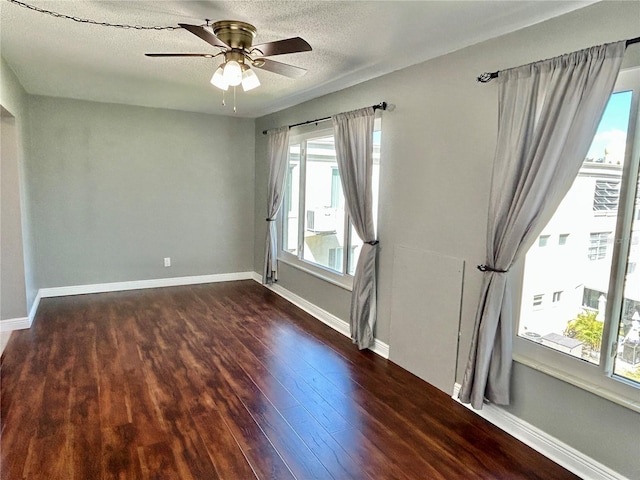 spare room featuring dark wood-type flooring, ceiling fan, a textured ceiling, and plenty of natural light