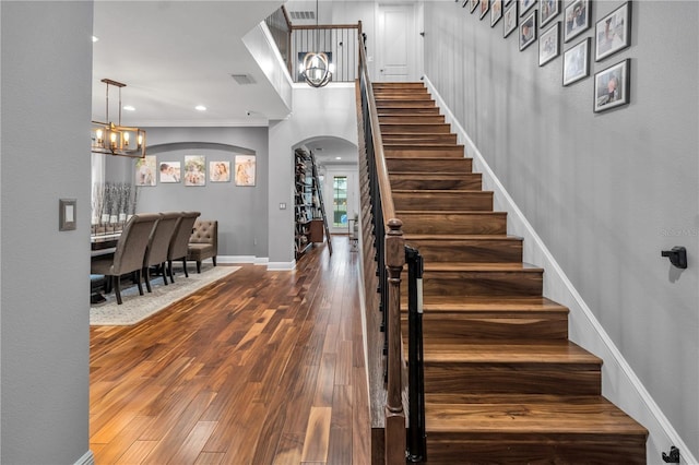 stairway featuring ornamental molding, hardwood / wood-style floors, and an inviting chandelier