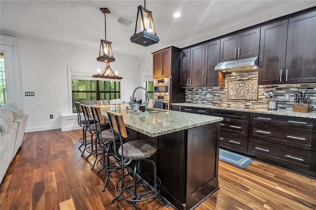 kitchen with an island with sink, pendant lighting, dark brown cabinetry, and stainless steel double oven