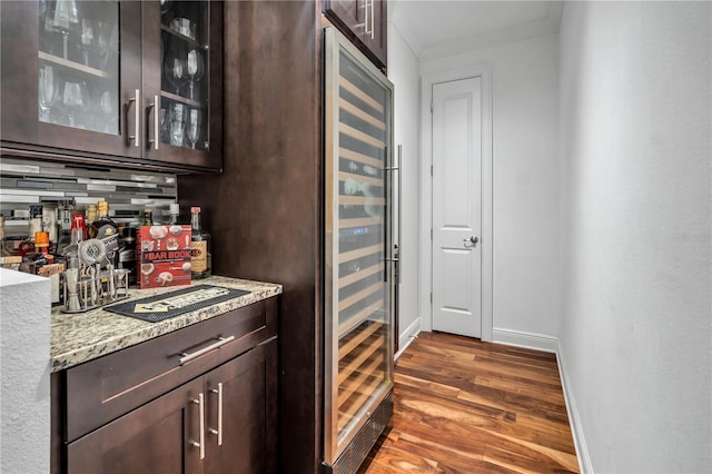 bar with crown molding, dark brown cabinets, beverage cooler, and backsplash