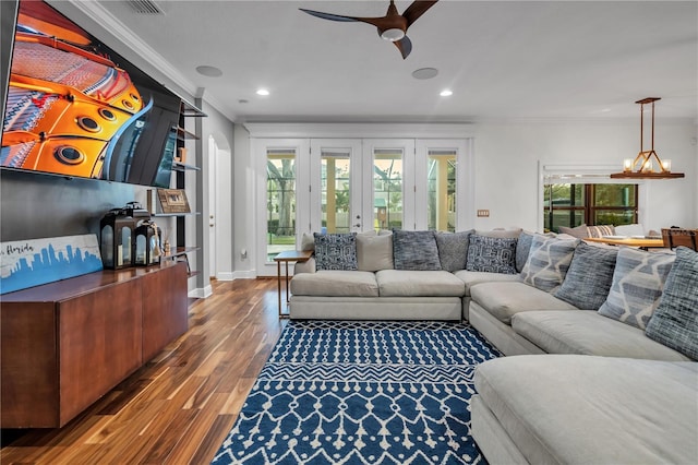 living room featuring dark wood-type flooring, ornamental molding, ceiling fan with notable chandelier, and french doors