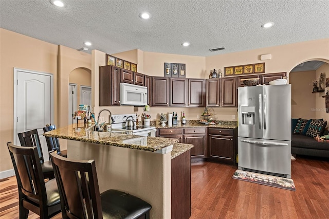 kitchen with white appliances, a textured ceiling, dark hardwood / wood-style flooring, and dark brown cabinetry