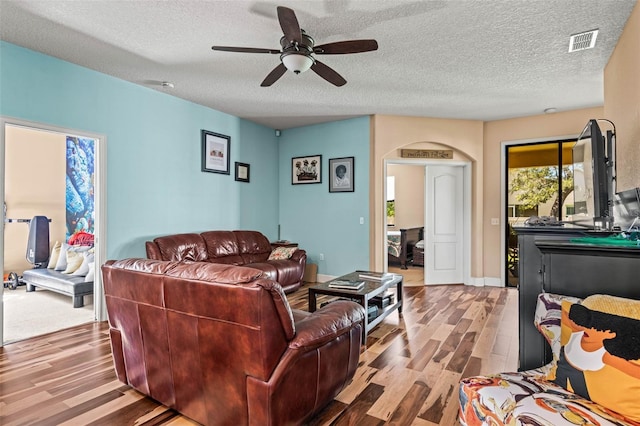 living room featuring light hardwood / wood-style flooring, a textured ceiling, and ceiling fan