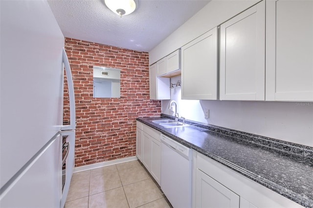 kitchen featuring white appliances, sink, a textured ceiling, white cabinetry, and brick wall