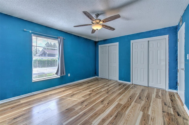 unfurnished bedroom featuring light hardwood / wood-style flooring, a textured ceiling, multiple closets, and ceiling fan