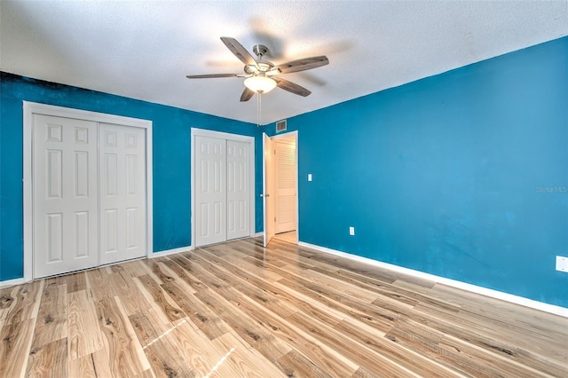 unfurnished bedroom with ceiling fan, multiple closets, a textured ceiling, and light hardwood / wood-style floors