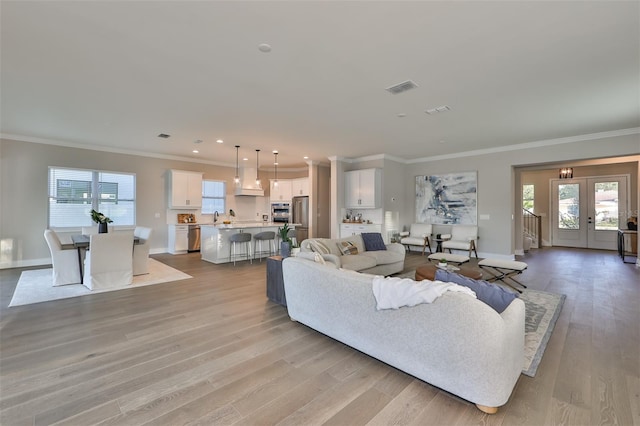 living room featuring sink, crown molding, light hardwood / wood-style flooring, and french doors