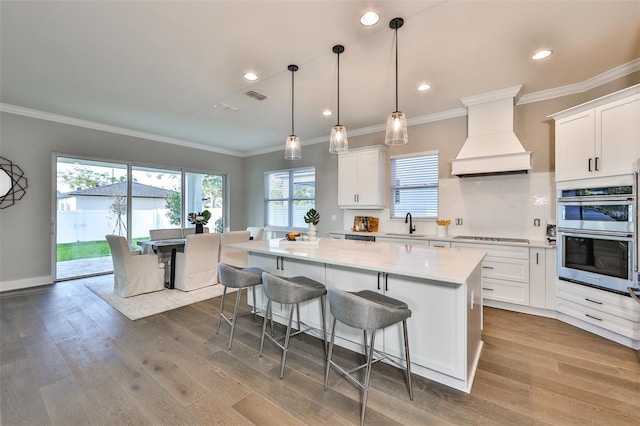 kitchen featuring light hardwood / wood-style floors, custom range hood, double oven, and a kitchen island