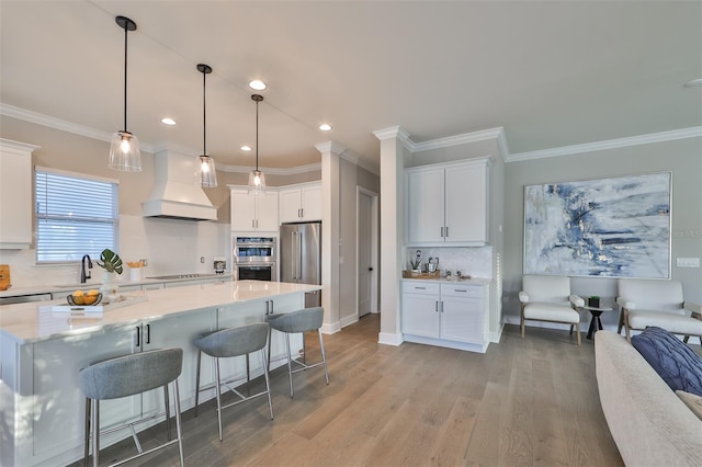 kitchen featuring premium range hood, white cabinets, pendant lighting, and light hardwood / wood-style floors