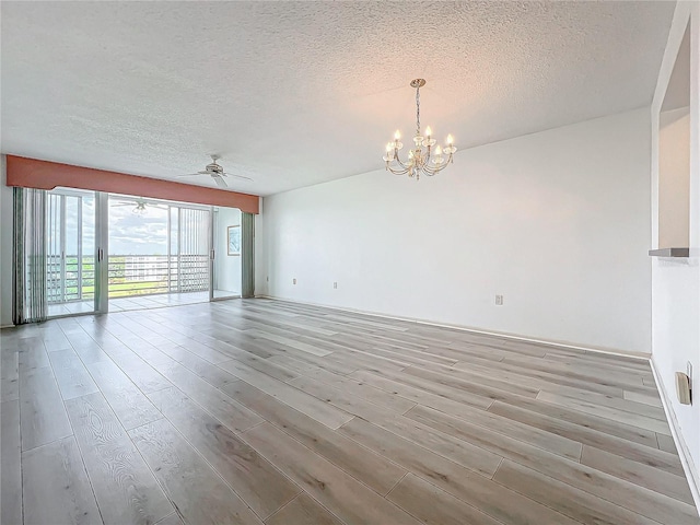 empty room featuring a textured ceiling, wood finished floors, and ceiling fan with notable chandelier