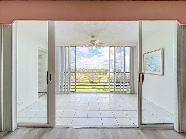 doorway featuring a wall of windows, light tile patterned floors, a ceiling fan, and a textured ceiling