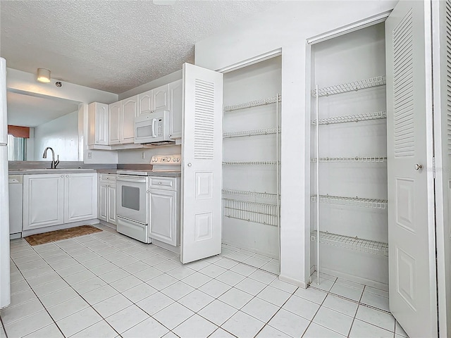 kitchen featuring white appliances, light tile patterned floors, a sink, a textured ceiling, and white cabinetry