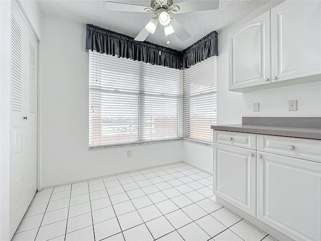 unfurnished dining area featuring light tile patterned flooring, a ceiling fan, and a textured ceiling