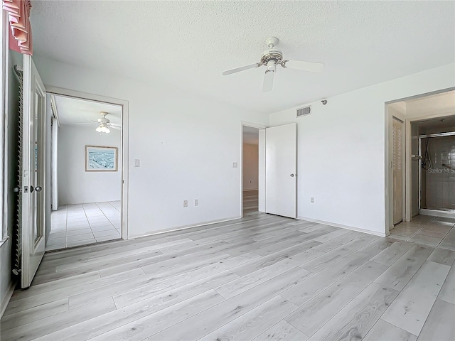 unfurnished bedroom with a ceiling fan, visible vents, light wood-style flooring, ensuite bathroom, and a textured ceiling