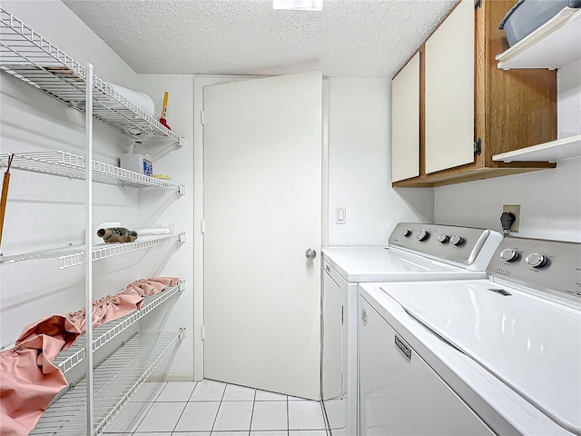 laundry area featuring light tile patterned floors, washing machine and dryer, cabinet space, and a textured ceiling