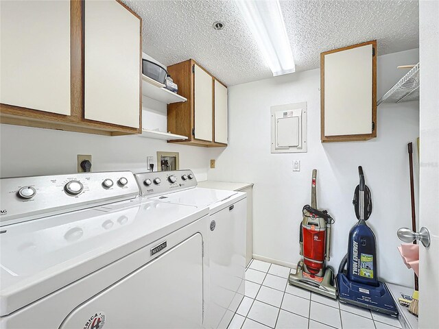 washroom featuring electric panel, a textured ceiling, washing machine and dryer, cabinet space, and light tile patterned flooring