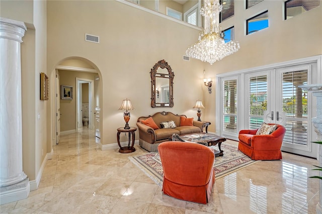 living room featuring a towering ceiling, french doors, a chandelier, and decorative columns