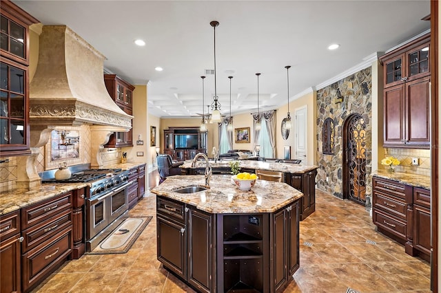 kitchen featuring sink, an island with sink, stainless steel appliances, decorative light fixtures, and light stone counters