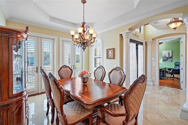 dining room with an inviting chandelier, crown molding, ornate columns, and a raised ceiling