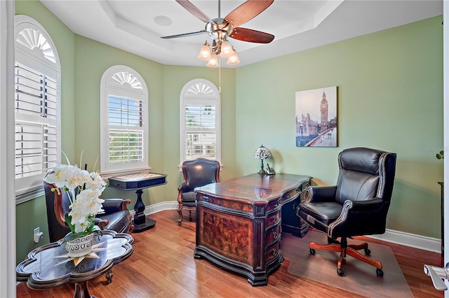 home office featuring ceiling fan, wood-type flooring, and a raised ceiling