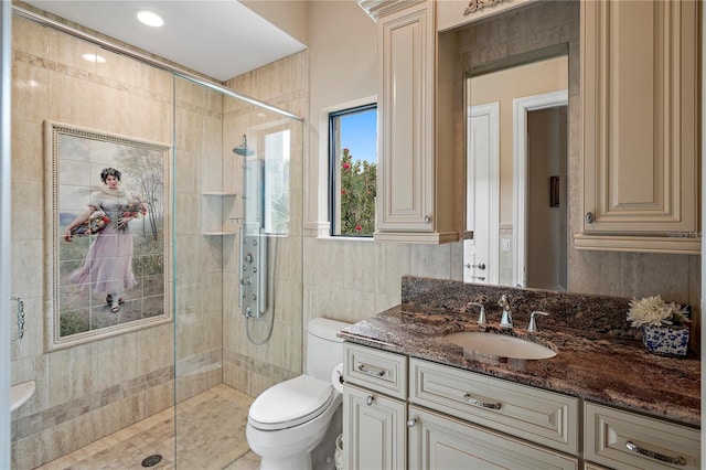 bathroom featuring a shower with door, tile walls, toilet, ornate columns, and vanity