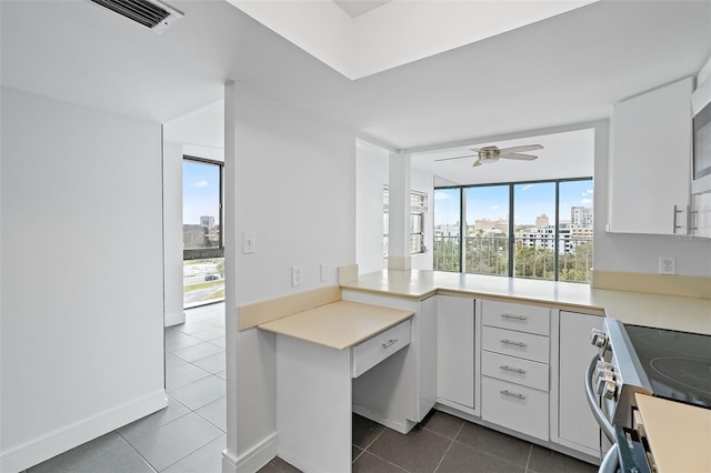 kitchen featuring dark tile patterned floors, stainless steel range with electric cooktop, white cabinetry, a wall of windows, and ceiling fan