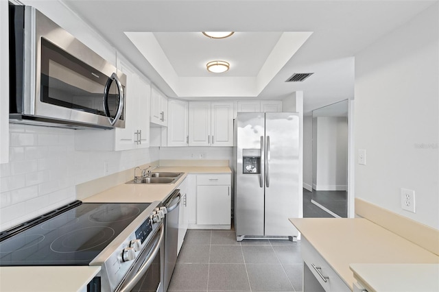 kitchen with white cabinetry, stainless steel appliances, backsplash, a tray ceiling, and sink