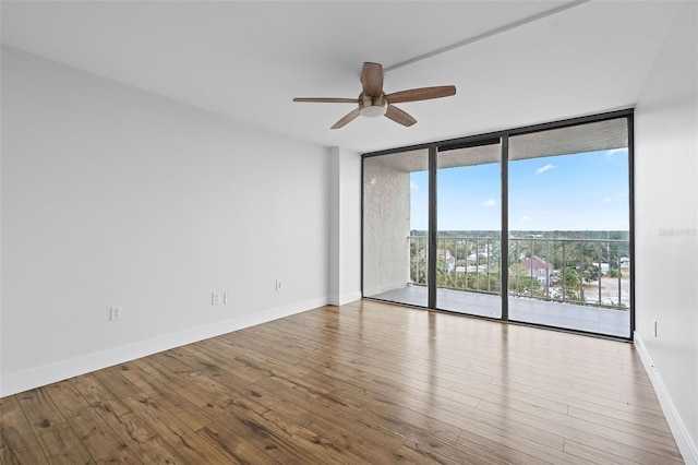 empty room with ceiling fan, a wall of windows, and light hardwood / wood-style floors