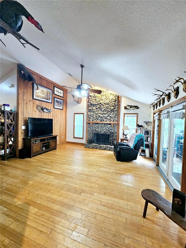 living room featuring a textured ceiling, vaulted ceiling, a fireplace, and light wood-type flooring