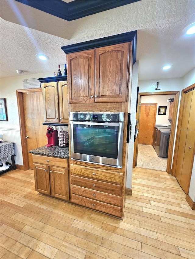 kitchen featuring oven, washer / clothes dryer, a textured ceiling, dark stone countertops, and light hardwood / wood-style floors