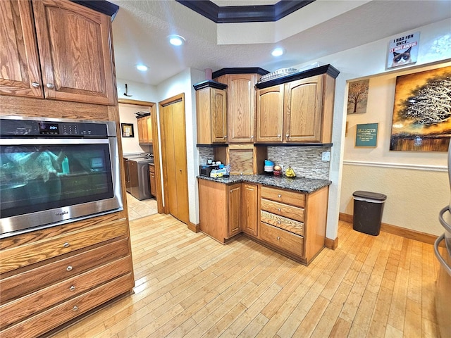 kitchen featuring tasteful backsplash, oven, dark stone counters, and light wood-type flooring