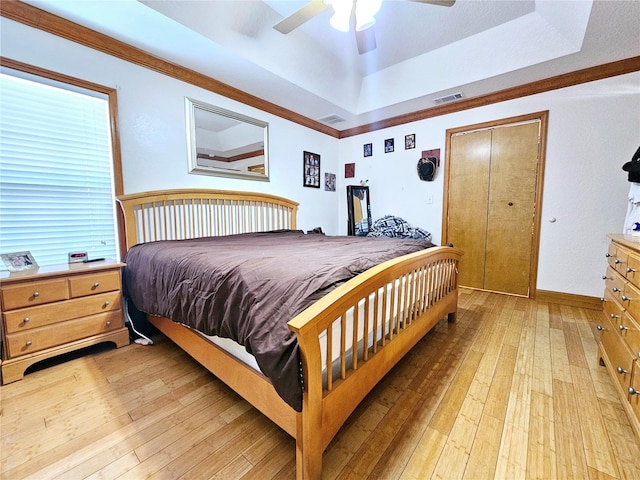 bedroom featuring light hardwood / wood-style flooring, a tray ceiling, a closet, and ceiling fan