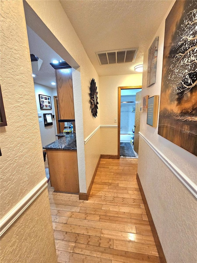 hall with light hardwood / wood-style flooring and a textured ceiling