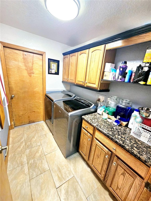 laundry area with cabinets, a textured ceiling, light tile patterned flooring, and washing machine and clothes dryer