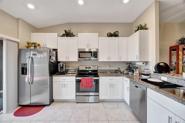 kitchen with lofted ceiling, white cabinetry, light stone counters, and stainless steel appliances