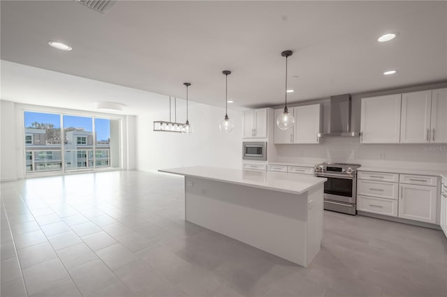 kitchen featuring wall chimney exhaust hood, a center island, decorative light fixtures, white cabinetry, and appliances with stainless steel finishes