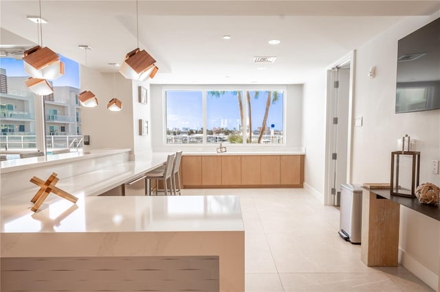 kitchen featuring light brown cabinetry, light tile patterned flooring, kitchen peninsula, and decorative light fixtures