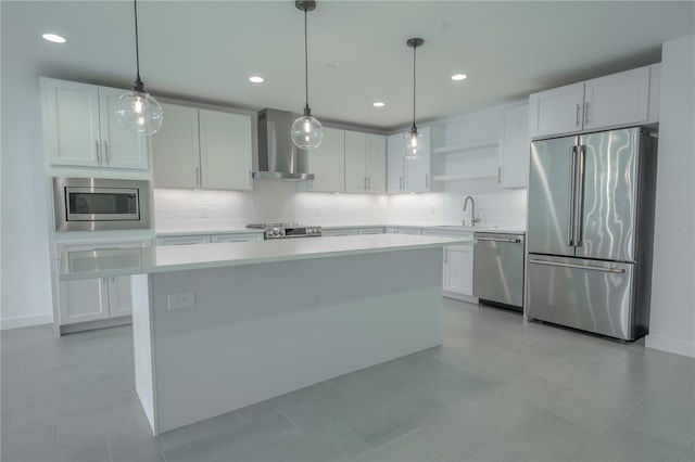 kitchen featuring hanging light fixtures, stainless steel appliances, wall chimney range hood, and white cabinets