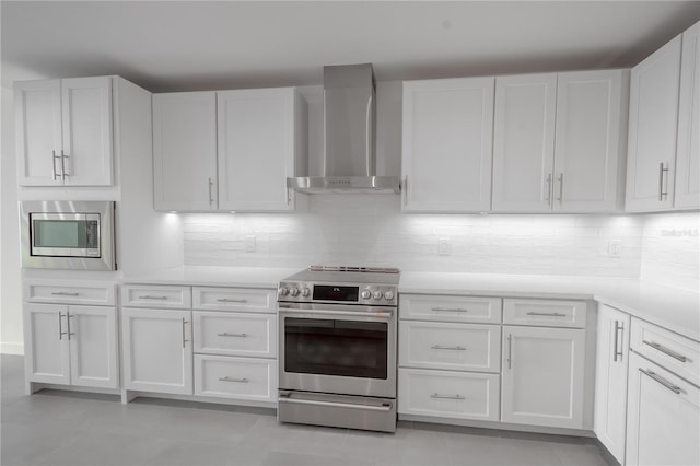 kitchen featuring tasteful backsplash, appliances with stainless steel finishes, wall chimney exhaust hood, white cabinets, and light tile patterned floors