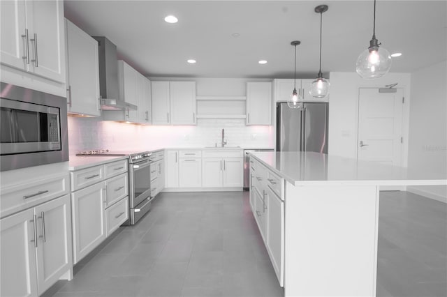 kitchen with wall chimney exhaust hood, white cabinets, stainless steel appliances, and hanging light fixtures